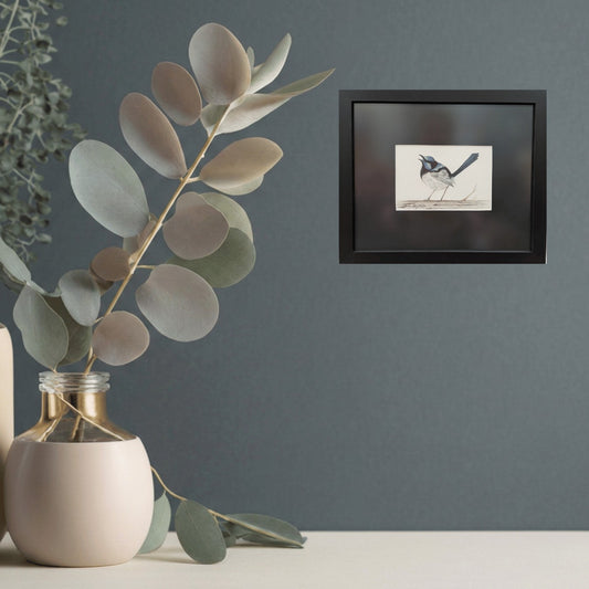 Framed artwork of a blue wren bird on a gray wall with a vase and eucalyptus leaves.