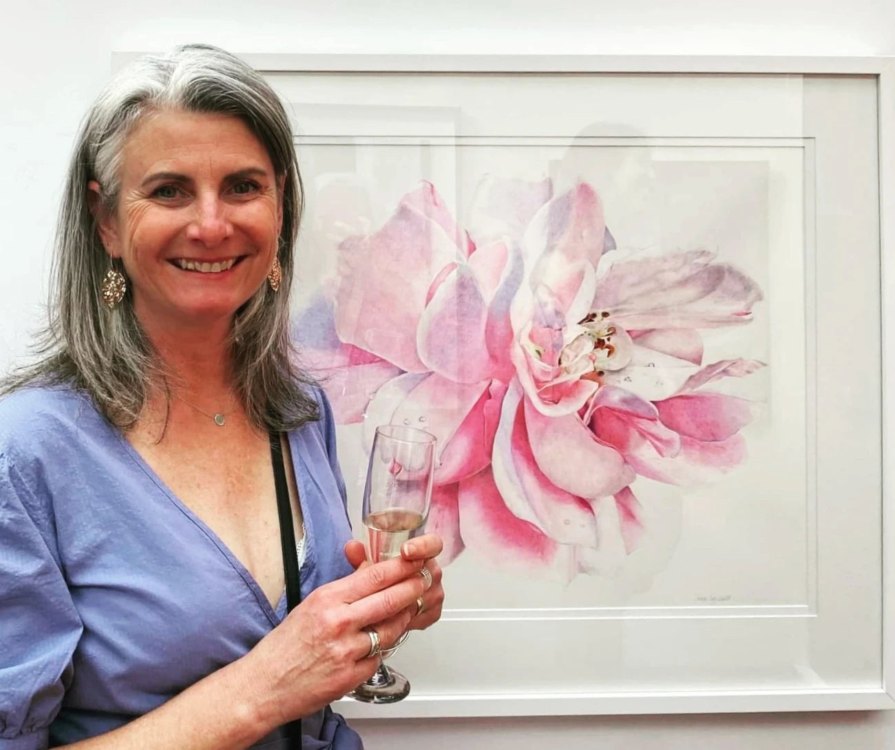 a photo of artist Jane Seychell in front of her colour pencil drawing of a pink peony rose