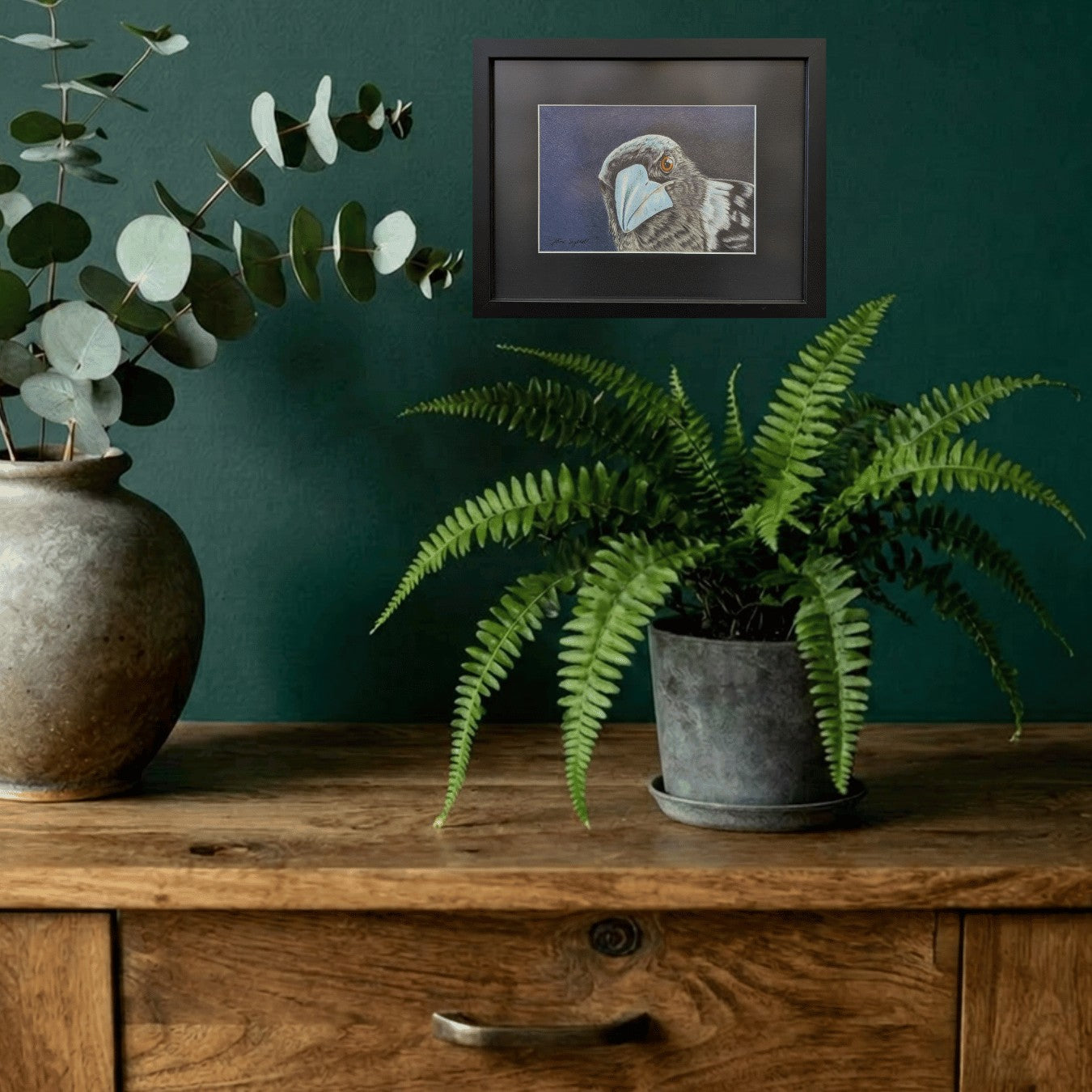 artwork of a magpie on a green wall above a wooden table top wit two green plants