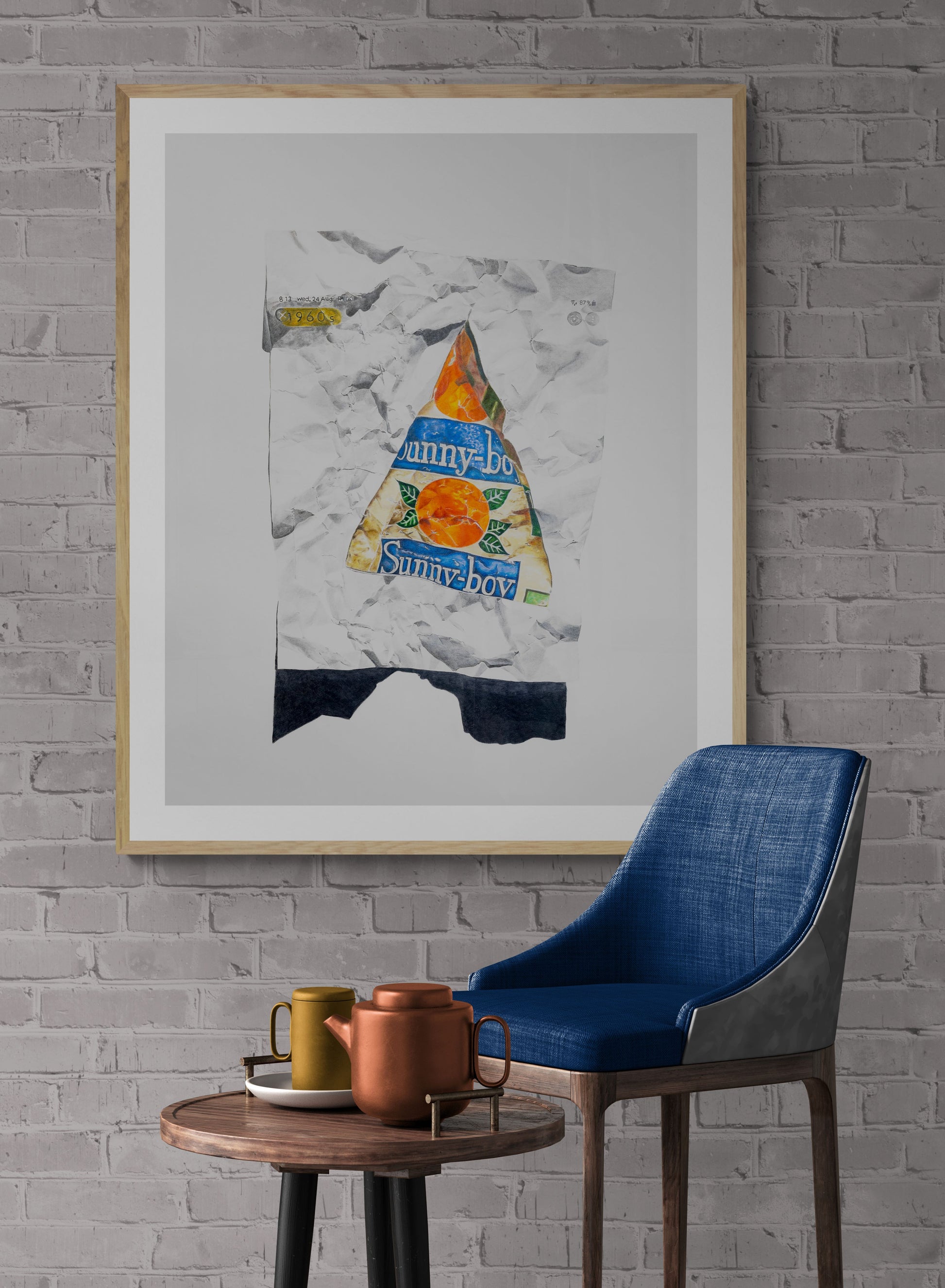 the photo is a framed drawing of a 1970s sunnyboy iceblock hanging on a wall with a blue chair and coffee table by artist Jane Seychell